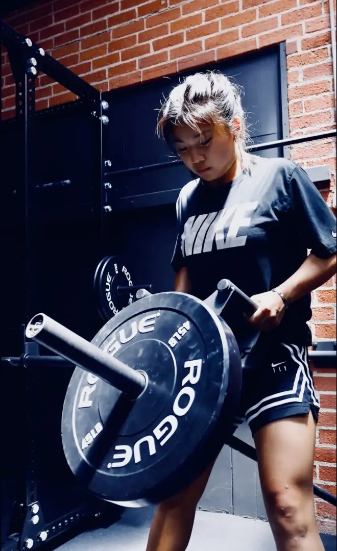 A woman is holding a barbell and looking at it.